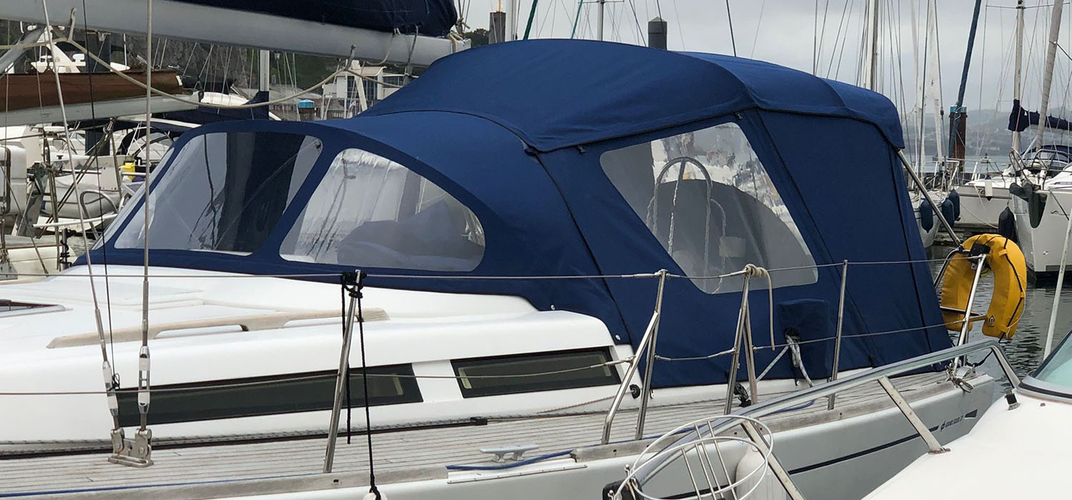 Cockpit and Enclosure Dark blue Sprayhoods and enclosure with windows, a bespoke design, patterned, measured and manufactured by Dart Sails and Covers, on the yacht cockpit in the marina